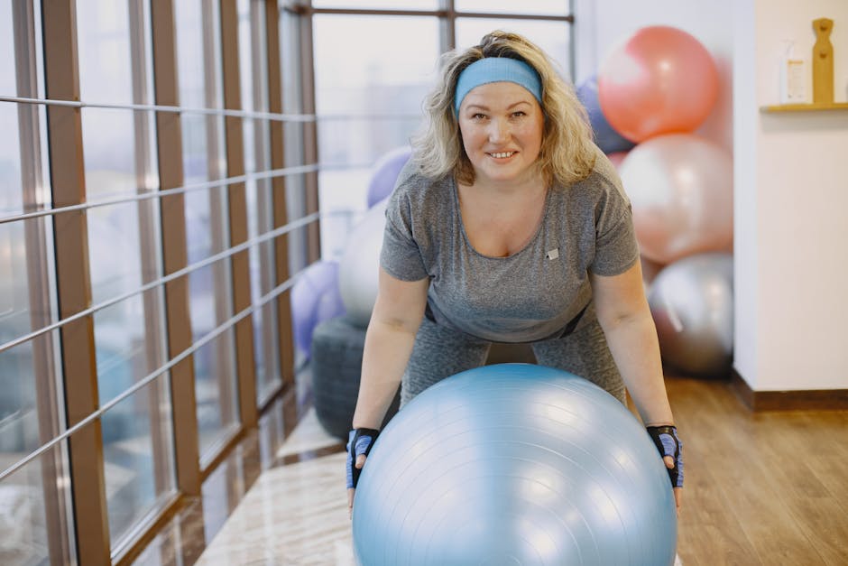 An adult woman engaging in a fitness workout with an exercise ball in a gym setting.